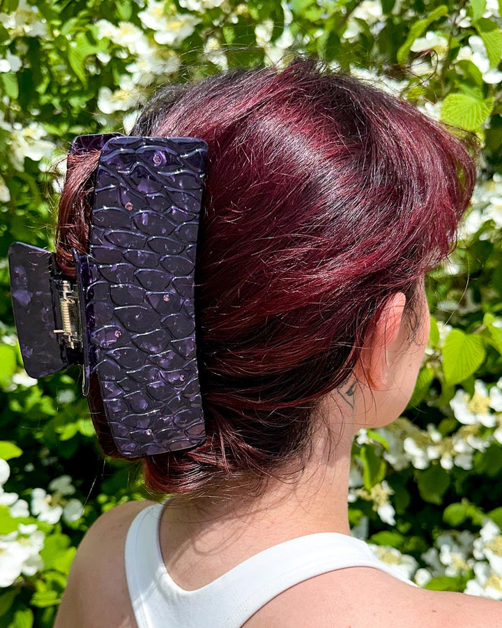 Hair clipped half-up-half-down with a purple pearlescent detailed bookish hair clip for fantasy readers designed to look like dragon scales with gem embellishments.