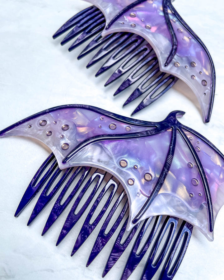 Close up of a fantasy hair accessory in the shape of dragon wings, featuring two combs in a purple pearlescent color and engraved details.