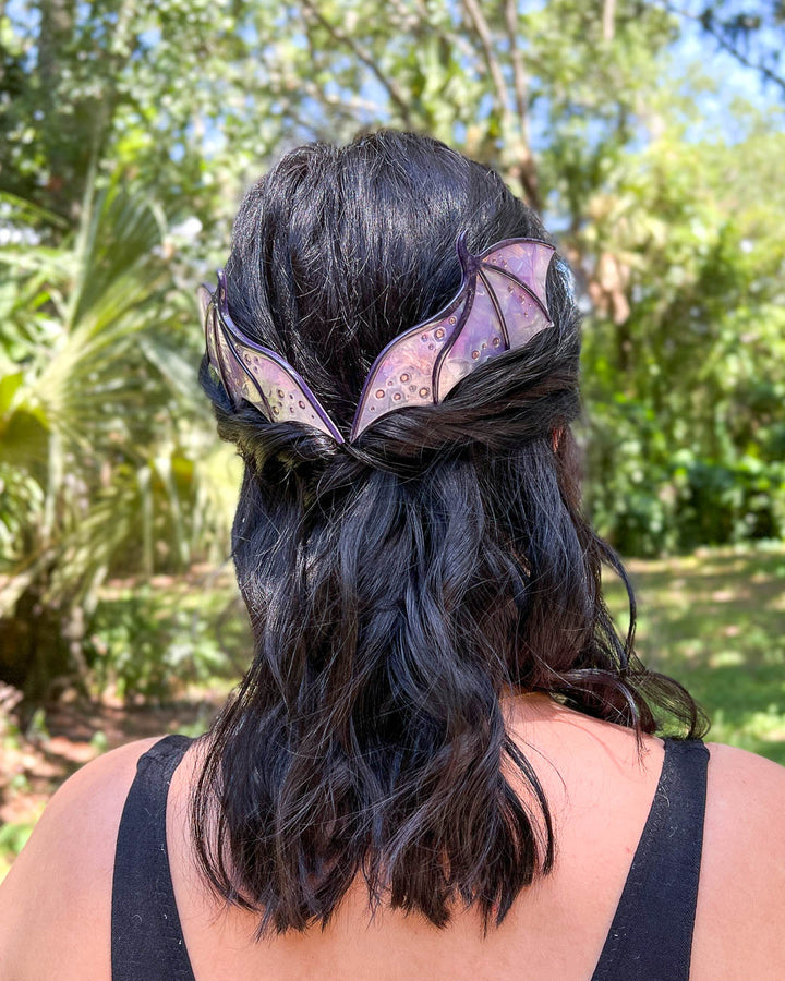 Fantasy hair combs featuring large combs in the shape of dragon wings in purple with engraved embellishments and a pearlescent color.