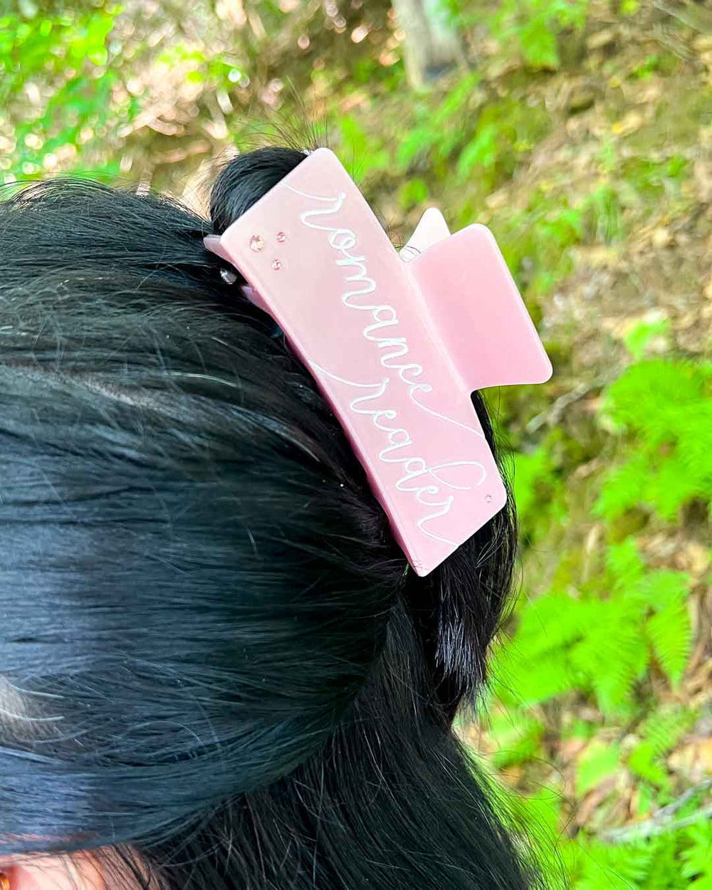 Bookish hair clip in light pink with 'romance reader' written in white script text with gem embellishments on the corners.