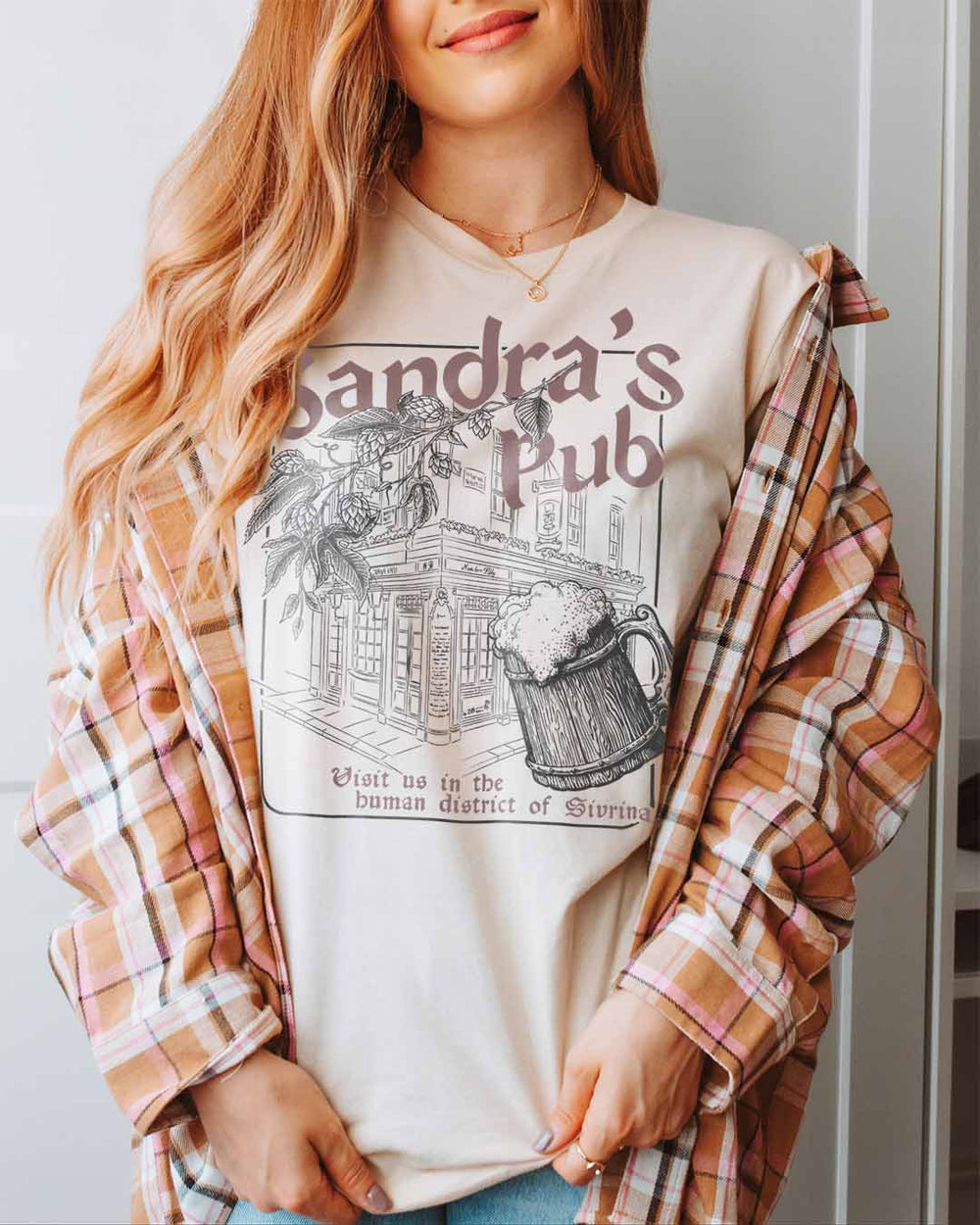 The Serpent and the Wings of Night tee designed with a storefront for Sandra's Pub with a full tankard and 'Visit us in the human district of Sivrinaj' written along the bottom.