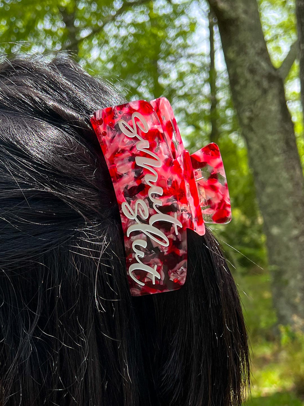 A red, pink, and transparent bookish hair clip with white script with the phrase 'smut slut.'