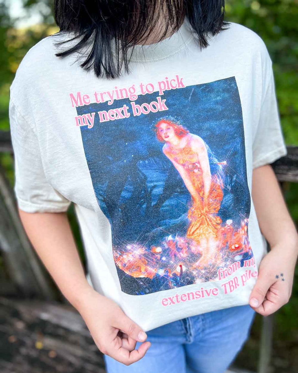 Bookish tee featuring a fine art painting of a woman peering forward with the quote, 'Me trying to pick my next book from my extensive TBR pile.'