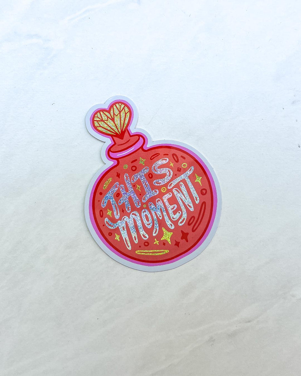 Emily Henry sticker for People We Meet on Vacation fans featuring glitter text saying 'This moment' on an illustrated perfume bottle.