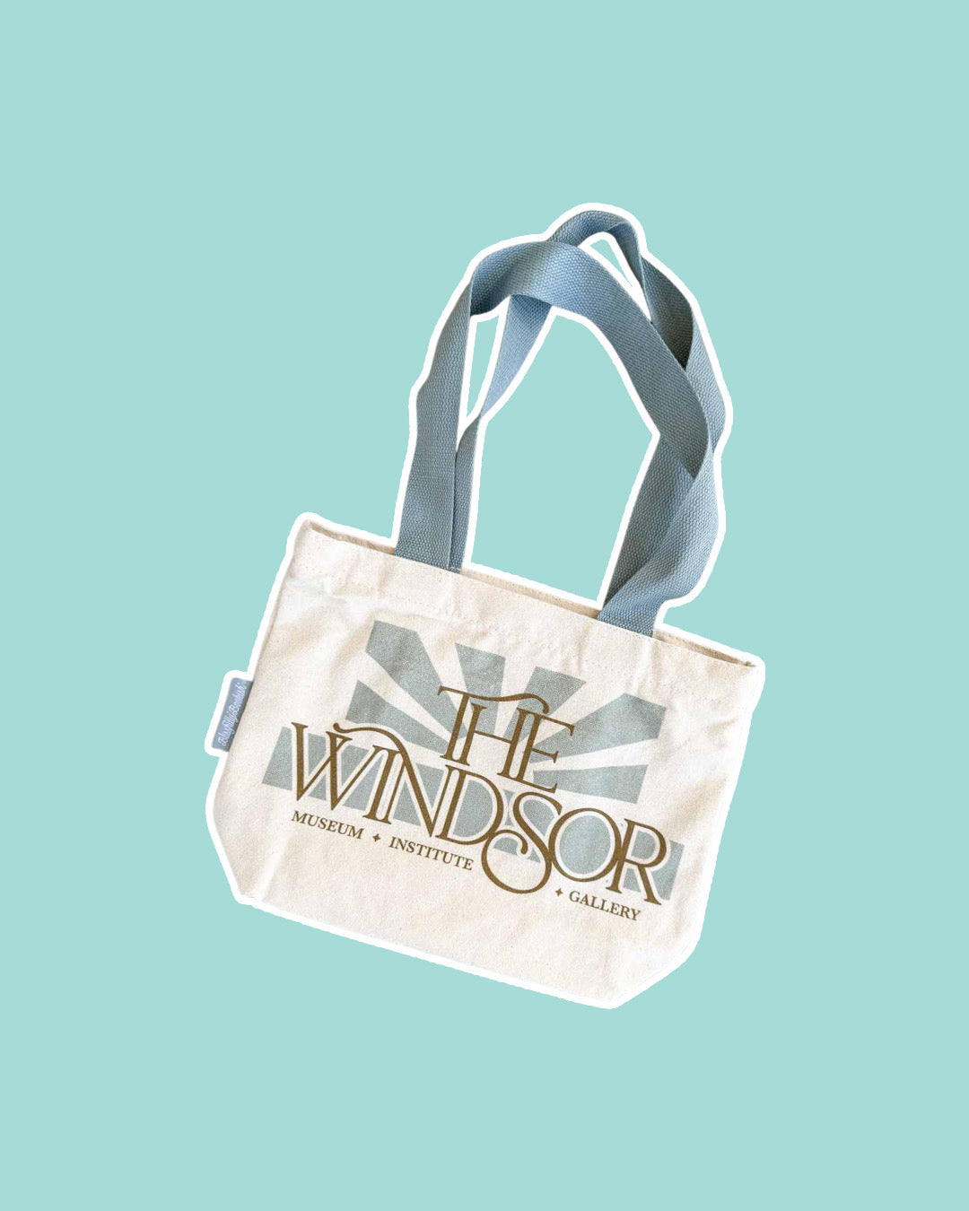 The Windsor Tote bag on blue background featuring block art of a rising sun and "the Windsor" written over it with "Museum. Institute. Gallery" along the bottom.