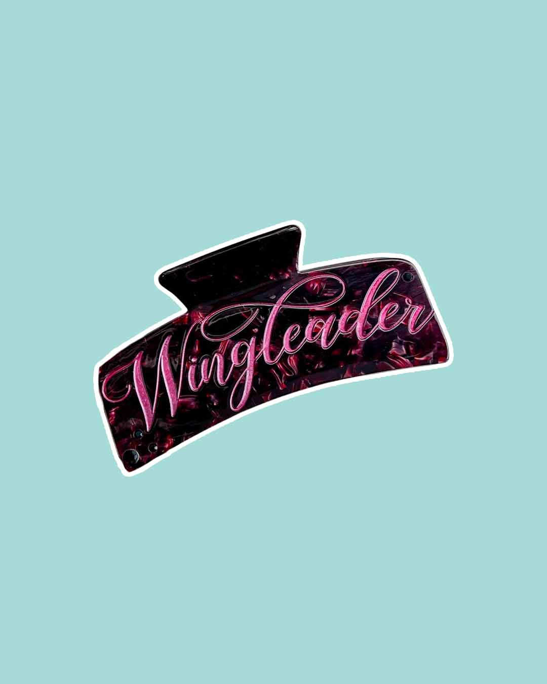 A bookish hair claw clip with maroon pearlescent detailing and 'wingleader' in vibrant pink script.