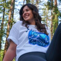 person sitting on a picnic table wearing leggings and night court inspired boardwalk airbrush tee in the woods