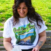 person sitting on a bench wearing the north bear shores beach read boardwalk airbrush inspired white boyfriend tee reading a book