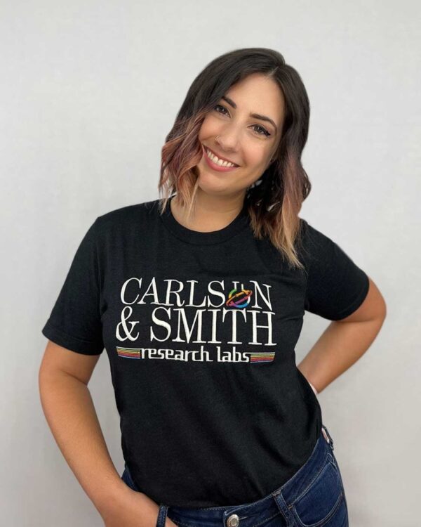 person wearing black boyfriend tee with carlsen and smith research labs embroidery standing against a white background with one hand on their hip and one through a belt loop