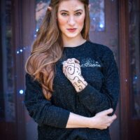 Model in front of a book case wearing a black long sleeve shirt with a white design on left chest