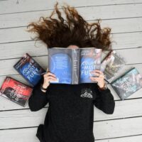 Model in front of a book case wearing a black long sleeve shirt with a white design on left chest