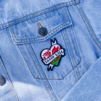Embroidered patch shaped like a heart with a Welsh dragon with the text "daddy will" on a denim jacket.