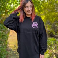 Model wearing long sleeve black shirt with purple design on left chest.