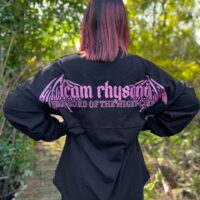 Model wearing long sleeve black shirt with purple design across shoulders.