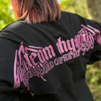 Model wearing long sleeve black shirt with purple design across shoulders.