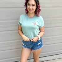 person wearing denim shorts with mint sky diamond farms shirt standing against white background