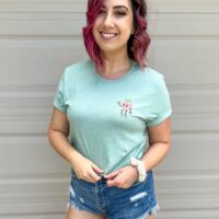 person wearing sky diamond farms tee shirt with the strawberry pocket print showing standing against a white wall smiling