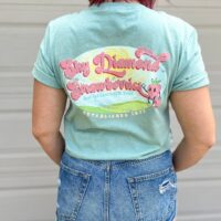 person wearing jean shorts and sky diamond farms tee shirt with back to the camera showing the sky diamond farms logo standing against a white wall