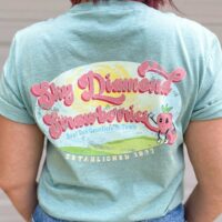 person wearing sky diamond farms tee shirt with back to the camera showing the sky diamond farms logo standing against a white wall