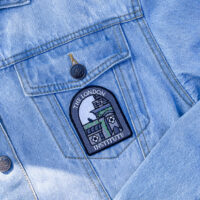 Embroidered patch shaped with the text "the london institute" and gray building on a denim jacket.
